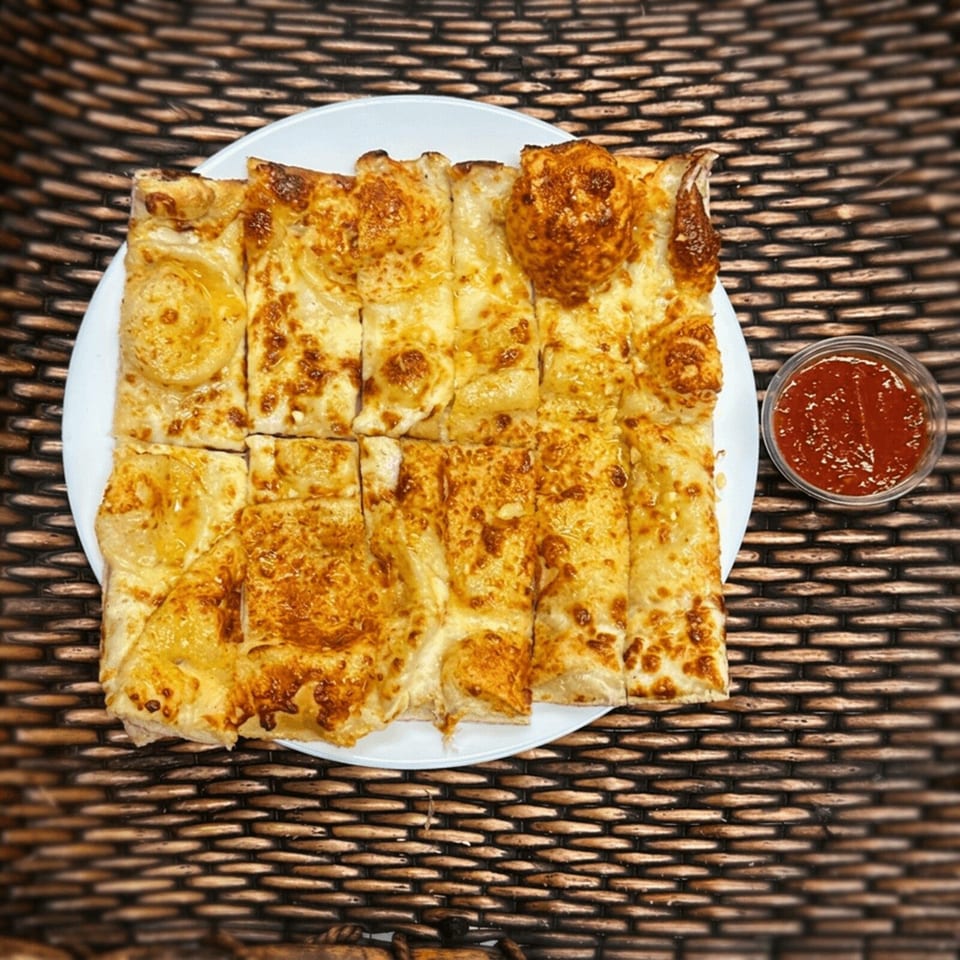 Golden-browned folded flatbread pieces arranged on a white plate with a small bowl of red dipping sauce.